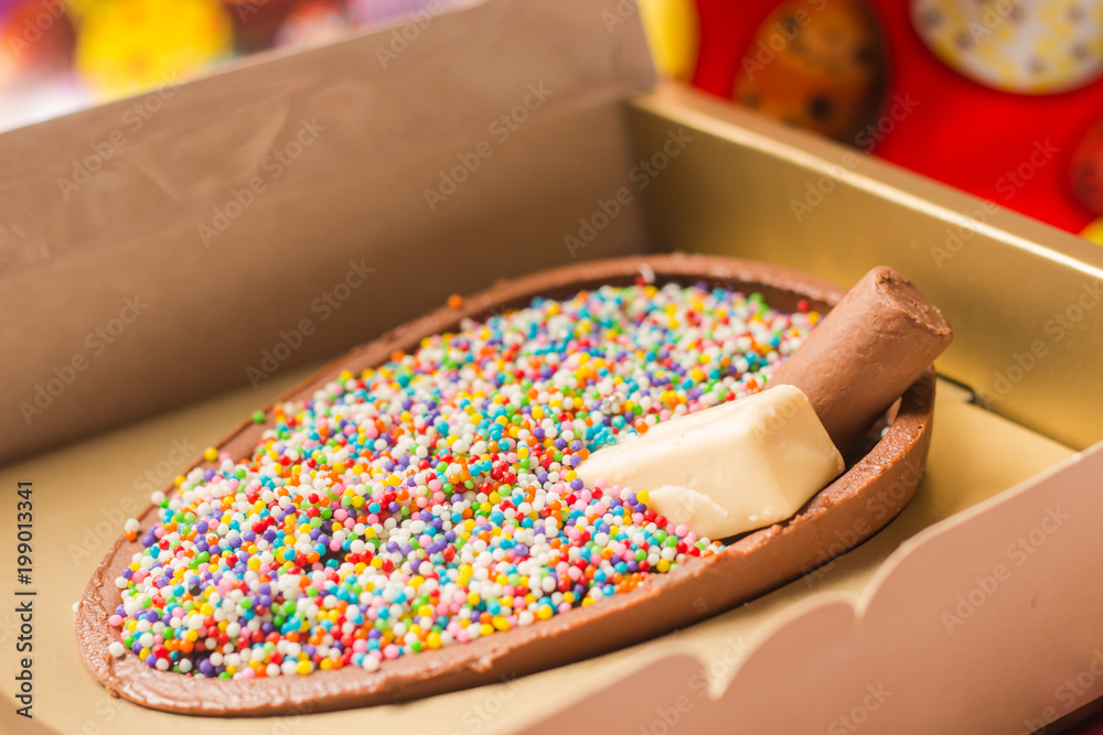 Feliz páscoa com ovo de chocolate confeitado dentro da caixa, cheia de bolinhas de chocolate.