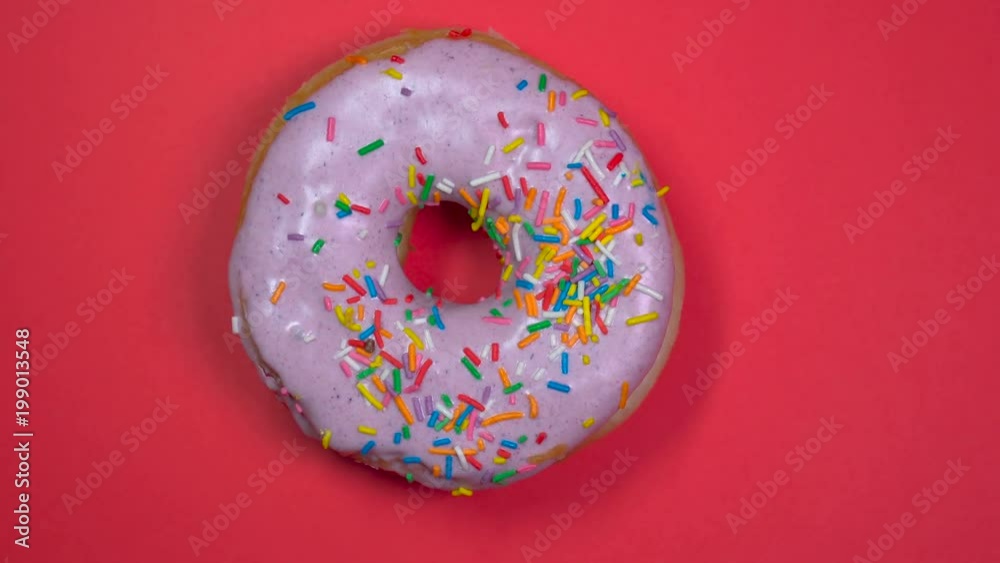 Bright and colorful sprinkled donut close-up macro shot spinning on a red background. Bright and colorful sprinkled donut close-up macro shot spinning on a red background.