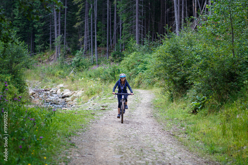 Young woman riding bike on forest trail road. Mountain bicycle trip background
