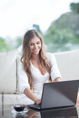 portrait of young woman sitting on sofa with laptop in summer house environment