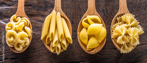 Different pasta types in wooden spoons on the table. Top view.