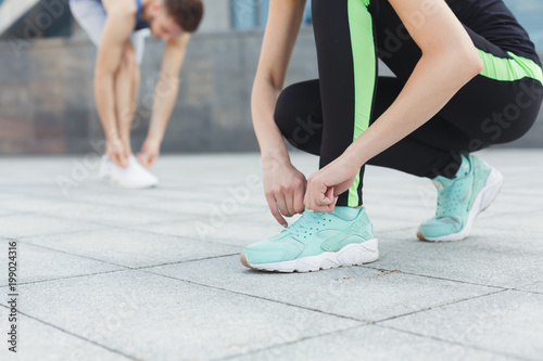 Unrecognizable man and woman tying shoelaces before running