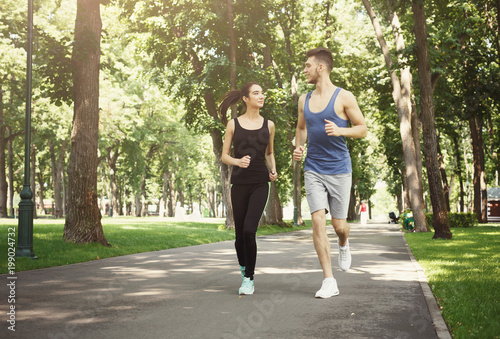 Fototapeta Naklejka Na Ścianę i Meble -  Young couple jogging in green park, copy space
