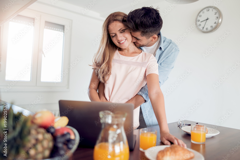 Happy young couple using laptop in the kitchen