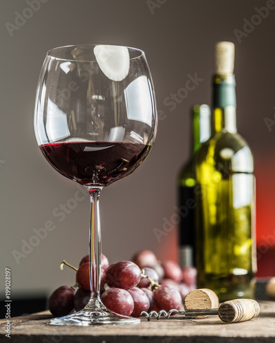 Glass of red wine on the table. Wine bottle and grapes at the background.
