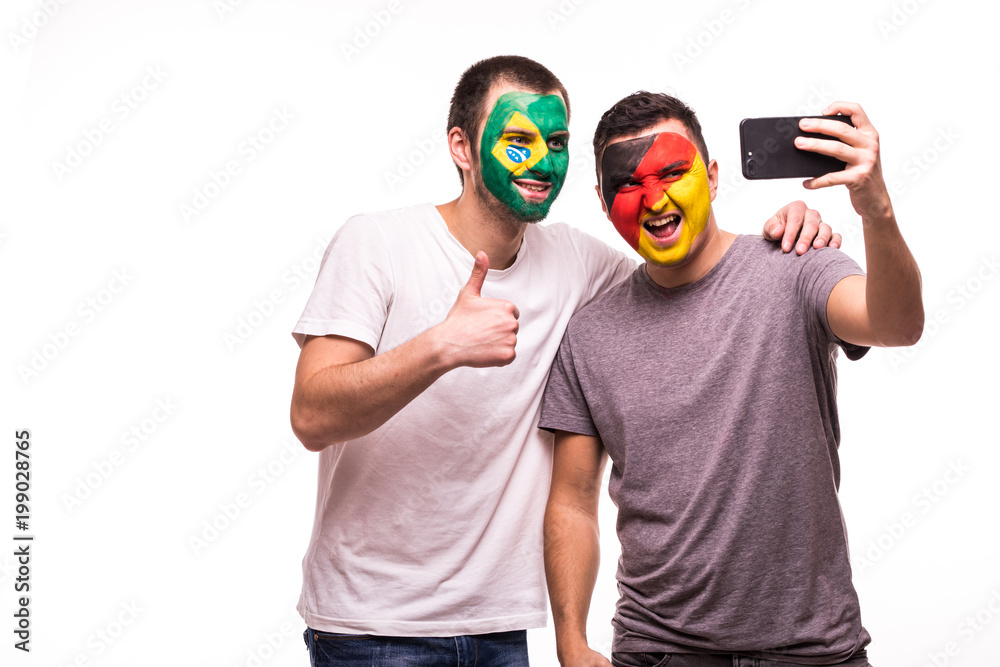 Football fans supporters with painted face of national teams of Brazil and Germany take selfie isolated on white background