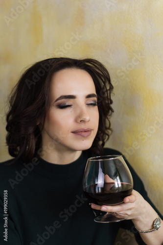 beautiful woman with closed eyes holds a glass of red wine and inhales its aroma