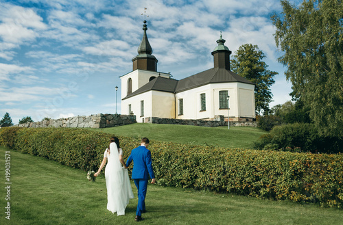 Wedding day. Bride and groom going to church through green field on blue sky backgrounds.