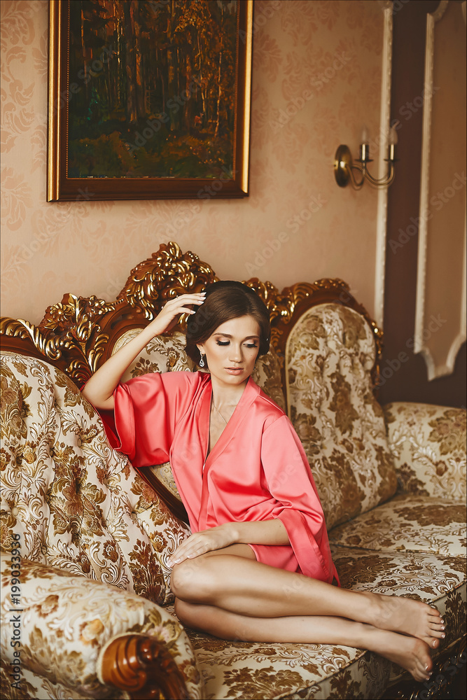 Fototapeta premium Beautiful and sexy brunette model girl in peignoir, posing on sofa at luxury interior
