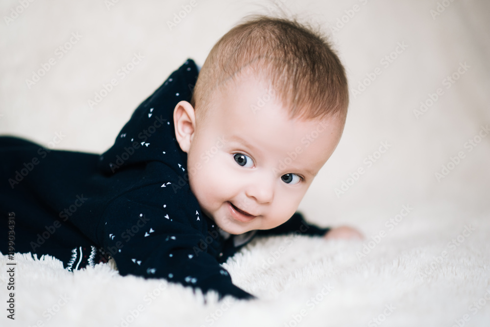 Small baby boy lying on stomach and raising his head awhile looking surprised and smiling cute, newborn