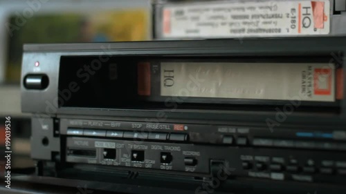 The hand takes a videocassette, inserts it into the video player and pushes the play