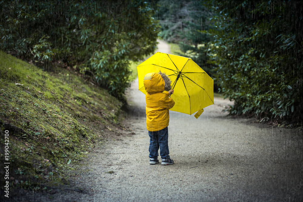 a kid in a park under a yellow umbrella in the rain
