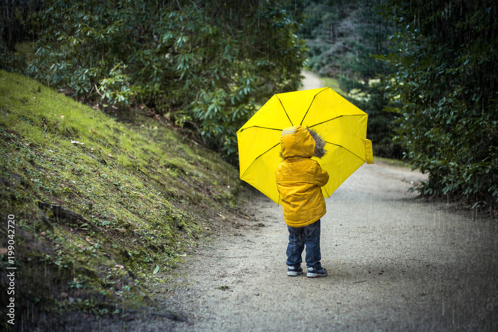 a kid in a park under a yellow umbrella in the rain