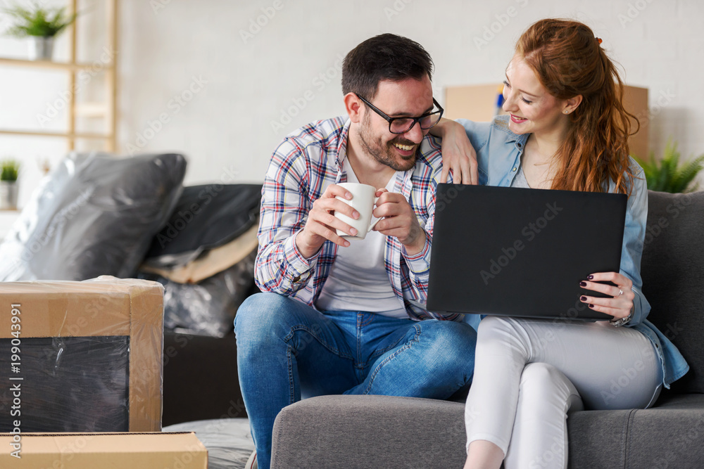 Young couple moving in new home. Sitting and relaxing after unpacking. Searching home decorating ideas on laptop. Young couple moving in new home. Sitting and relaxing after unpacking. Searching home decorating ideas on laptop.