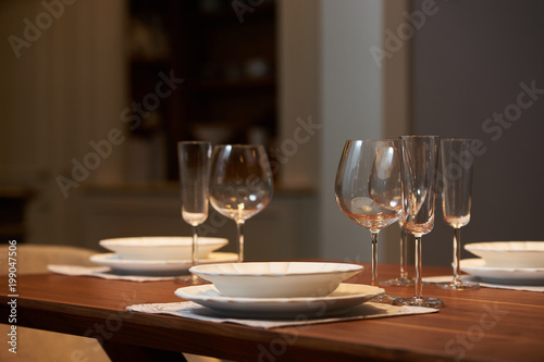 Luxury kitchen dining table setting, glasses, cutlery and wine in ice bucket. Modern kitchen interior with clean white plates, glasses and cutlery on wooden table