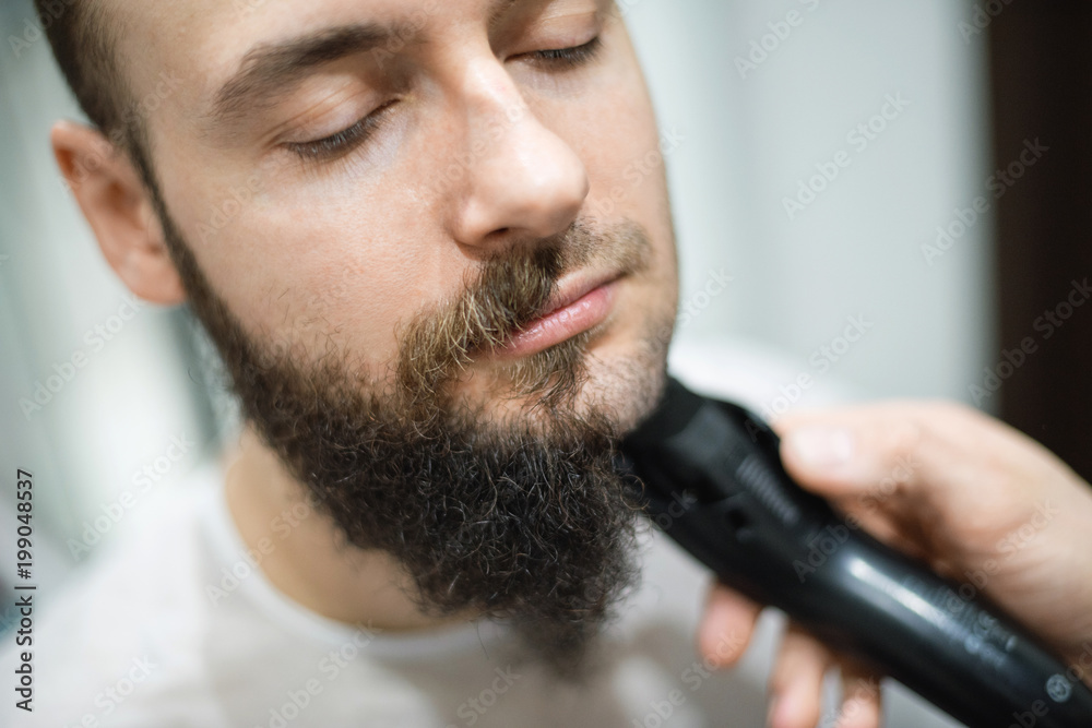 Handsome bearded man is getting shaved by hairdresser at the barbershop Handsome bearded man is getting shaved by hairdresser at the barbershop