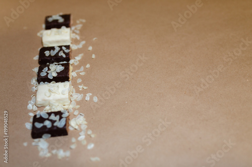 Snack chocolate protein bars with different flavors in the context of sprinkle rice flakes on baking paper, Teflon paper. Whey protein powder and chocolate protein bar on wooden background. Top view