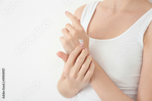 Young woman applying hand cream on white background, closeup