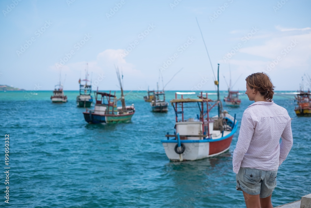 Caucasian woman standing on the beach of Midigama and looking on ocean and traditional colourful local boats, Travelling in Asia on vacation,
