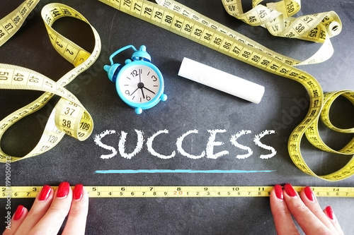 Success measurement concept with woman hands and yellow measurement tape on blackboard
