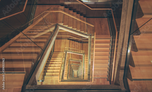 Spiral staircase from above with parquette floor. Square shaped stairs going downwards creating layers from each floor.