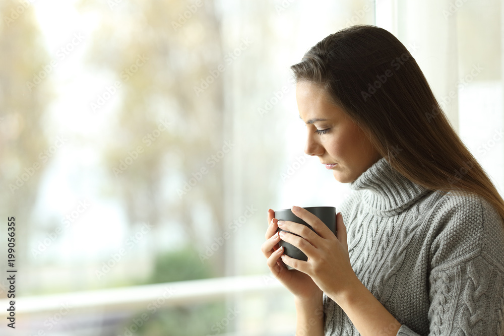 Sad melancholic woman holding a mug at home Sad melancholic woman holding a mug at home