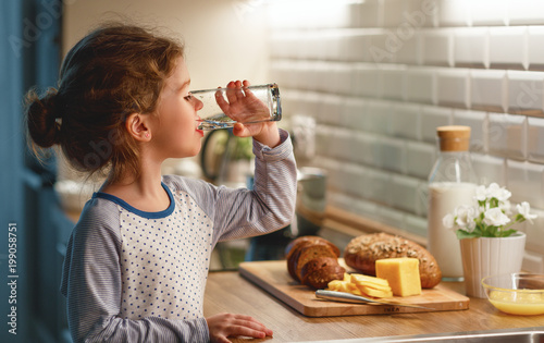 child girl is drinking water in kitchen at home