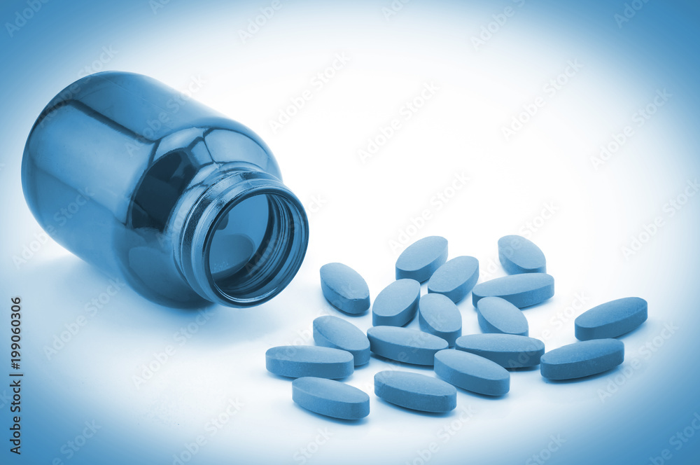 Pills of vitamin C spilled out open container in blue tone