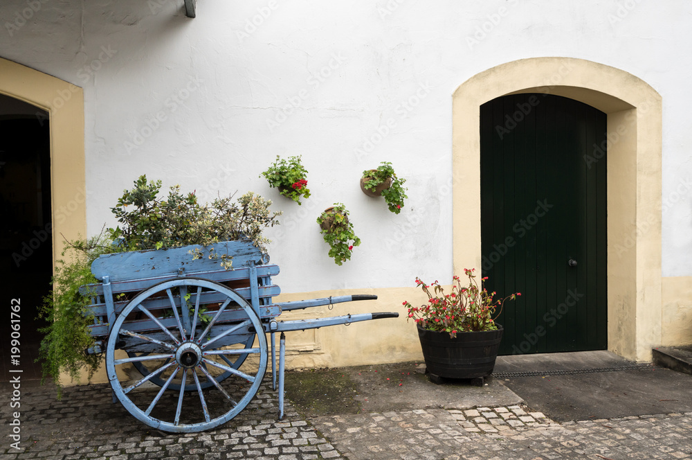 Old fashioned cart for horse with flowers by old white wall