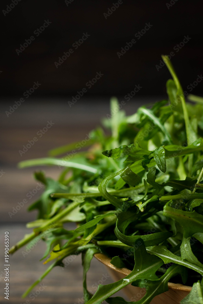 Fototapeta premium Fresh rucola with water droplets on a dark rustic background