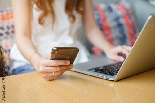 close up businesswoman hand using smartphone mobile and typing on laptop in office concept photo
