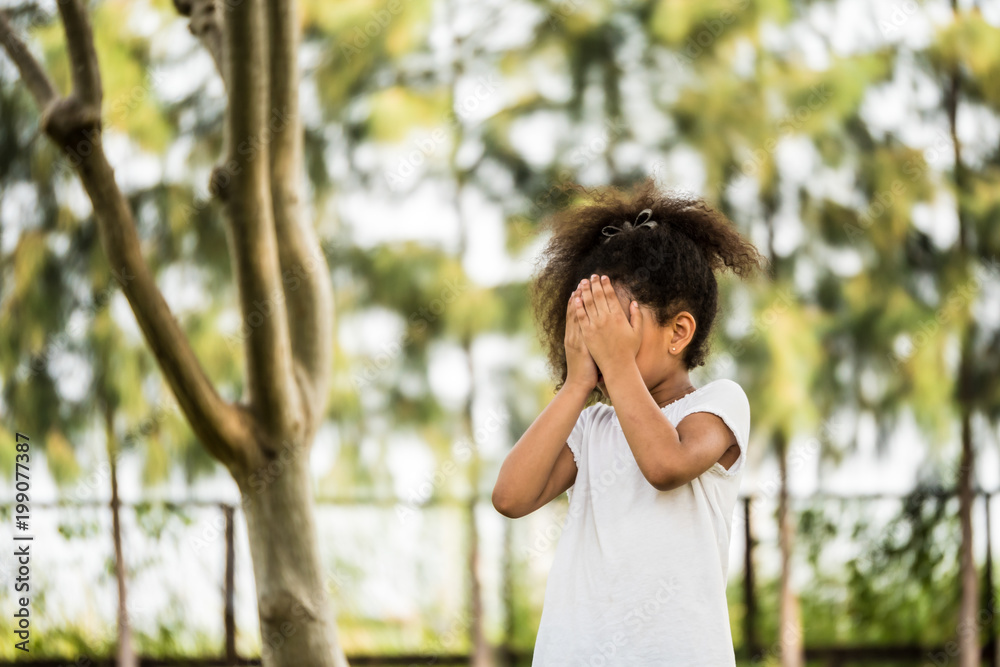 A Little girl is standing in a park, covering her face with her hands A Little girl is standing in a park, covering her face with her hands