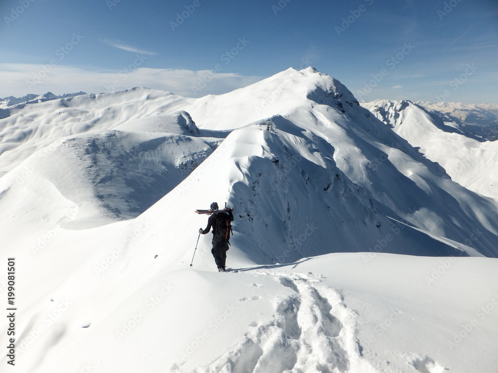 male backcountry skier traversing a narrow ridge and carrying his skis