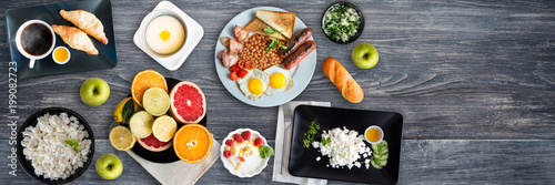 Different breakfasts on wooden table. Porridge, curd, fruits, croissants, yogurt, eggs, cottage cheese, apples, english breakfast. Top view, Copy space. Wide panoramic image.
