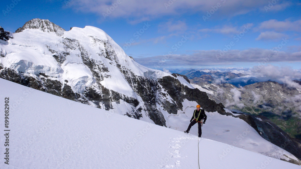male mountain climber on a high alpine glacier with a great view of the fantastic mountain landscape behind him