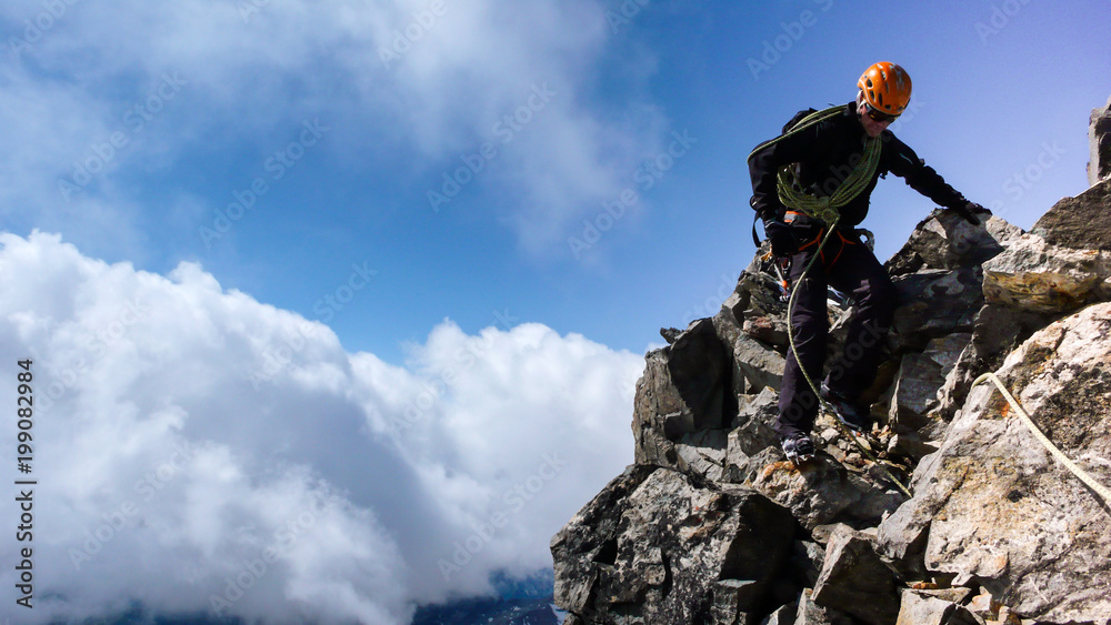 male mountain guide on a rock climbing route in the Alps under a blue sky