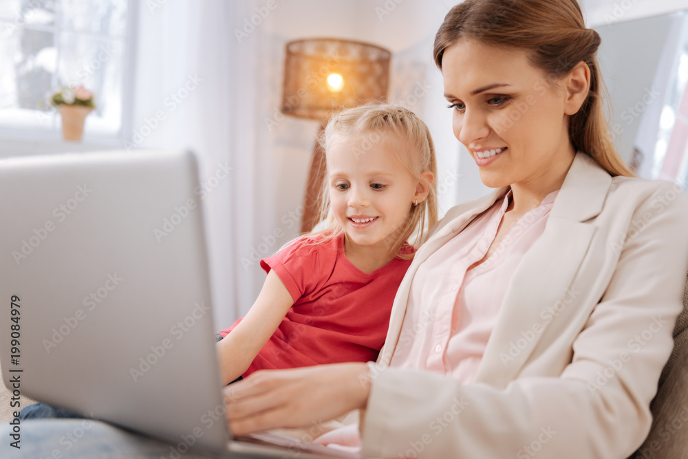 Digital innovations. Happy positive nice woman smiling and pressing a button while showing her daughter how to use the laptop Digital innovations. Happy positive nice woman smiling and pressing a button while showing her daughter how to use the laptop