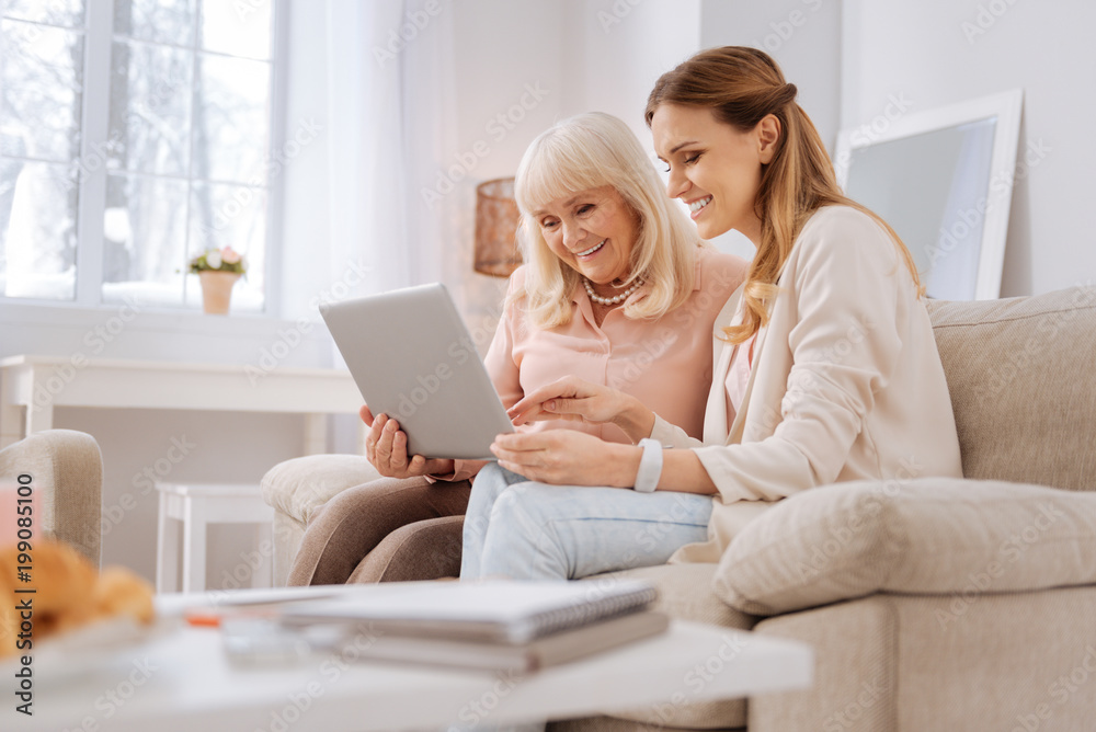 Smart technology. Nice joyful elderly woman sitting together with her daughter and smiling while learning how to use a laptop Smart technology. Nice joyful elderly woman sitting together with her daughter and smiling while learning how to use a laptop