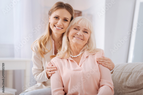 Happy family. Nice positive young woman smiling and looking at you while hugging her mother