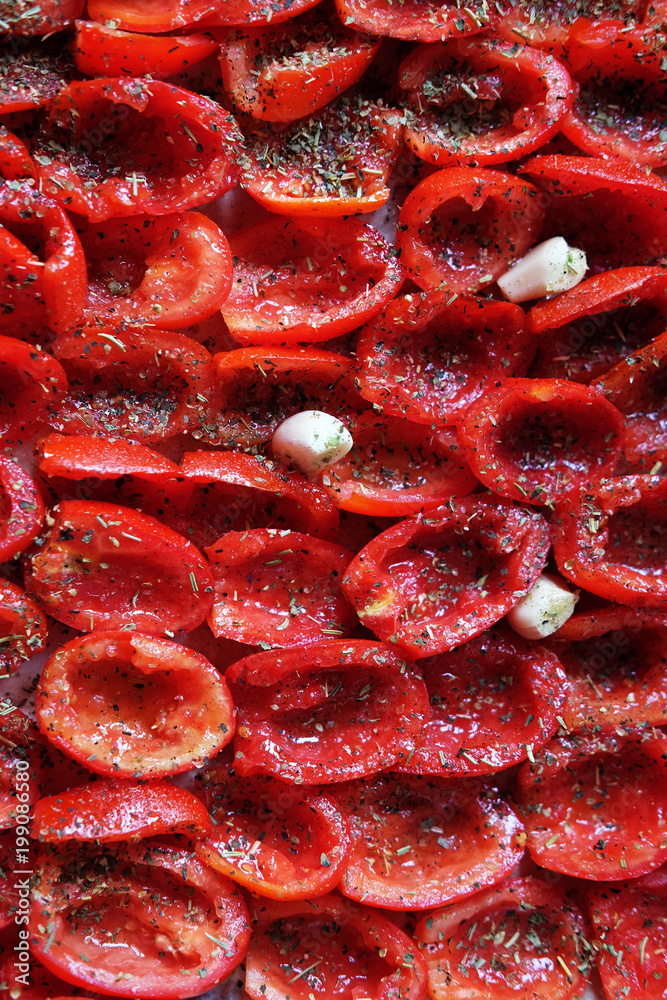 Tomatoes lie on a baking sheet, ready to bake. Sun-dried tomatoes with garlic. Food background. close up Tomatoes lie on a baking sheet, ready to bake. Sun-dried tomatoes with garlic. Food background. close up