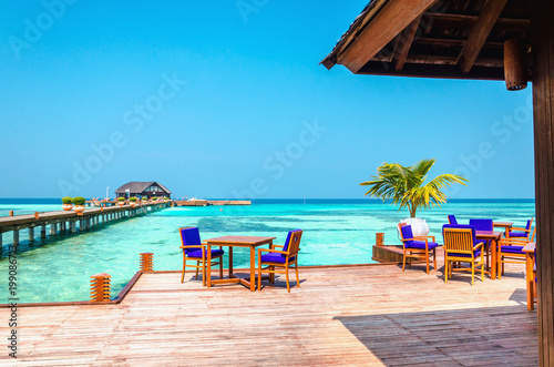 Tables and chairs in a wooden restaurant on stilts on the background of azure water and blue sky