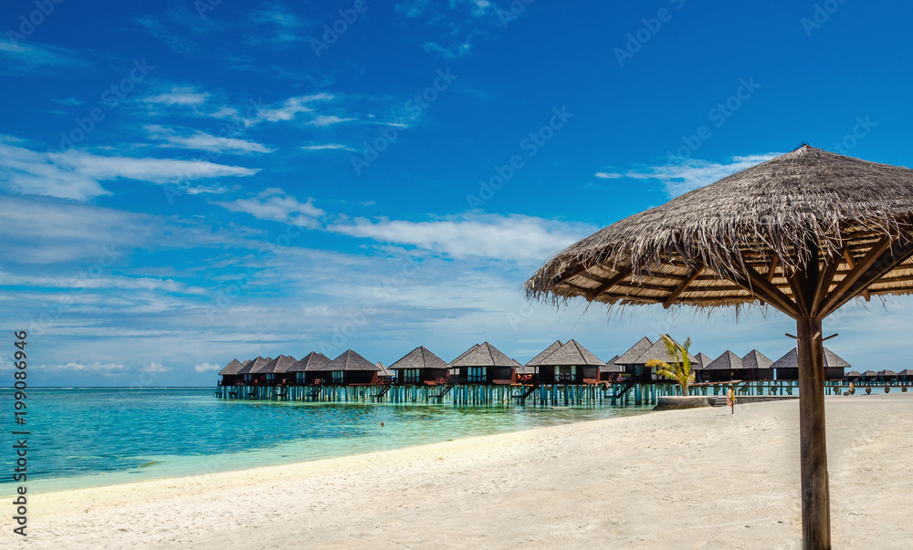 Wooden bungalow and palm tree umbrella on the background of azure water and blue sky, Maldives