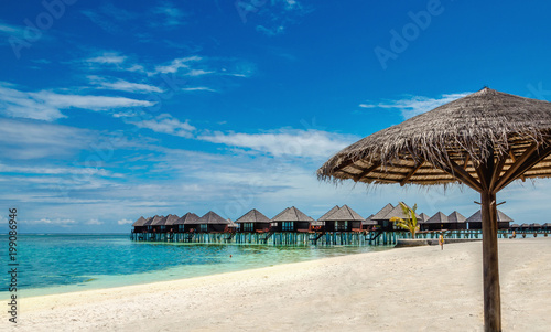 Wooden bungalow and palm tree umbrella on the background of azure water and blue sky  Maldives