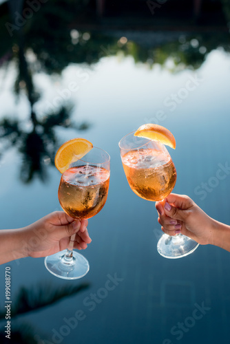Concept picture of a couple holding glasses of cocktail and cheers by the swiming pool to celebrate their success.
