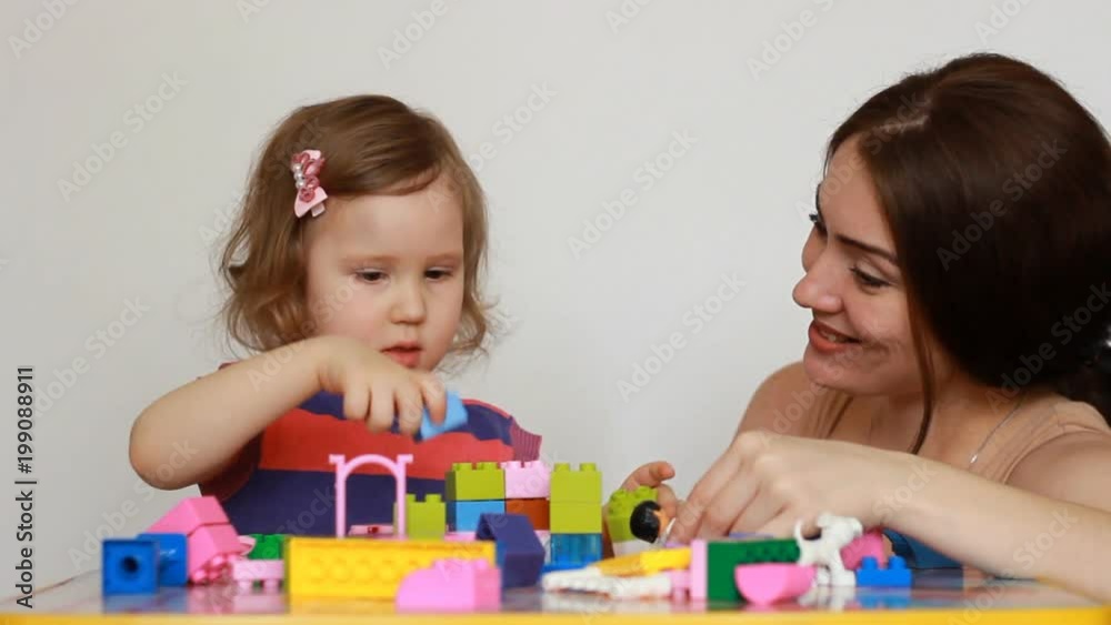 Educator and little girl playing together sitting at the table. Girl busy with his building constructor, teacher watching, talking and helps child. Development and education of preschoolers Educator and little girl playing together sitting at the table. Girl busy with his building constructor, teacher watching, talking and helps child. Development and education of preschoolers