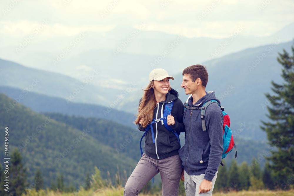 Young happy couple with backpack in mountains. Summer vacation tourism background with copy space. Warm color toned image
