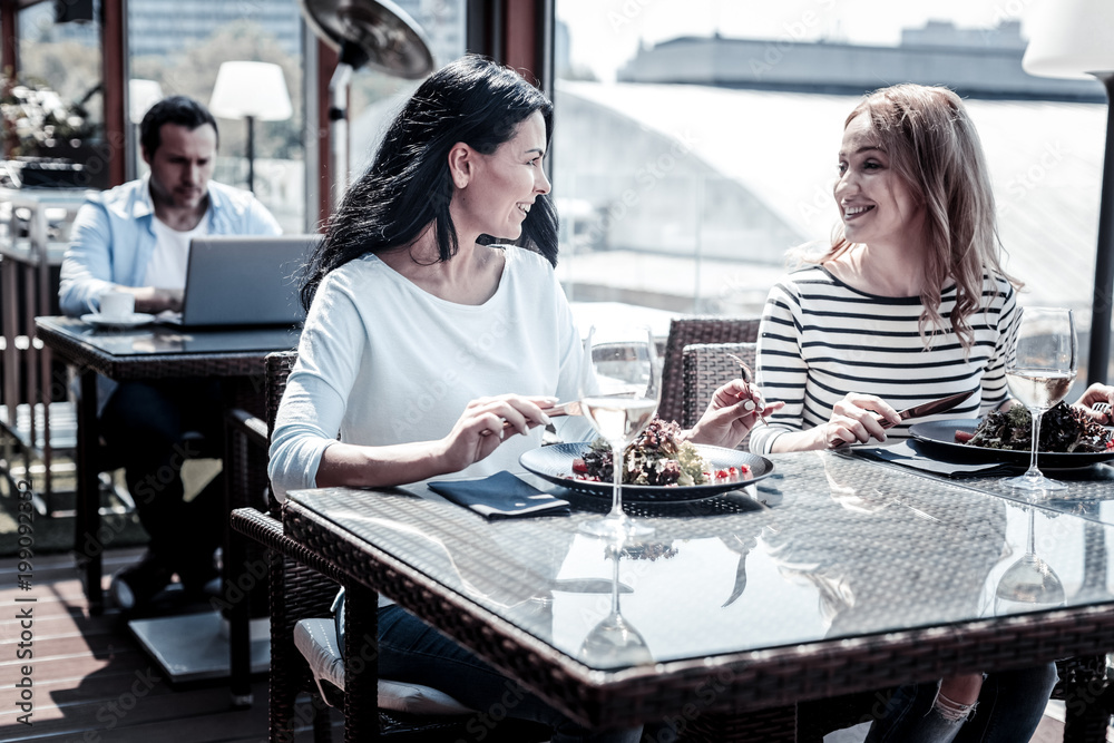 Our lunch. Joyful positive young women sitting at the table and looking at each other while enjoying their lunch Our lunch. Joyful positive young women sitting at the table and looking at each other while enjoying their lunch
