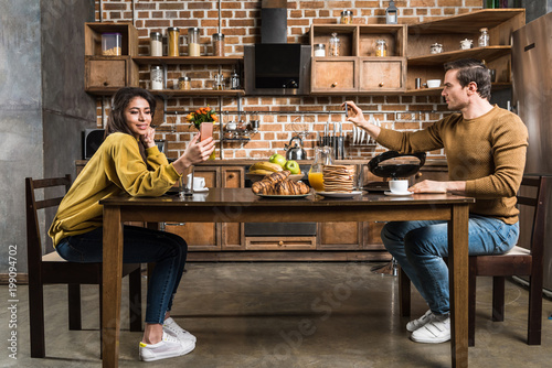 side view of multiethnic couple using smartphones during breakfast