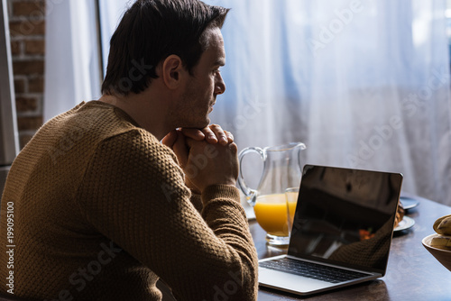side view of man using laptop with blank screen at home
