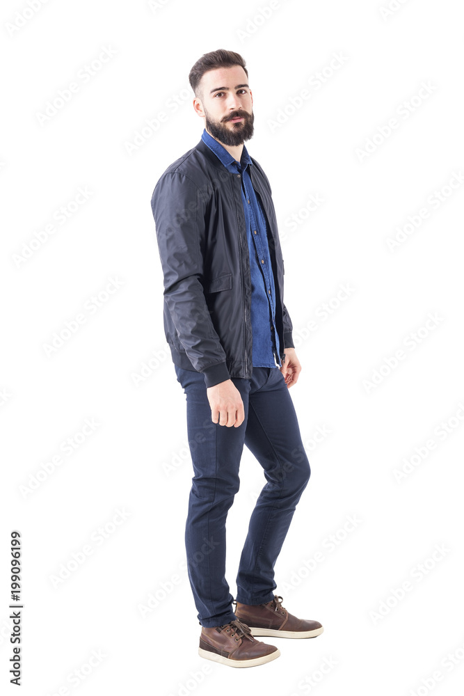 Side view of confident relaxed macho guy in bomber jacket posing and looking at camera. Full body isolated on white background. Side view of confident relaxed macho guy in bomber jacket posing and looking at camera. Full body isolated on white background.